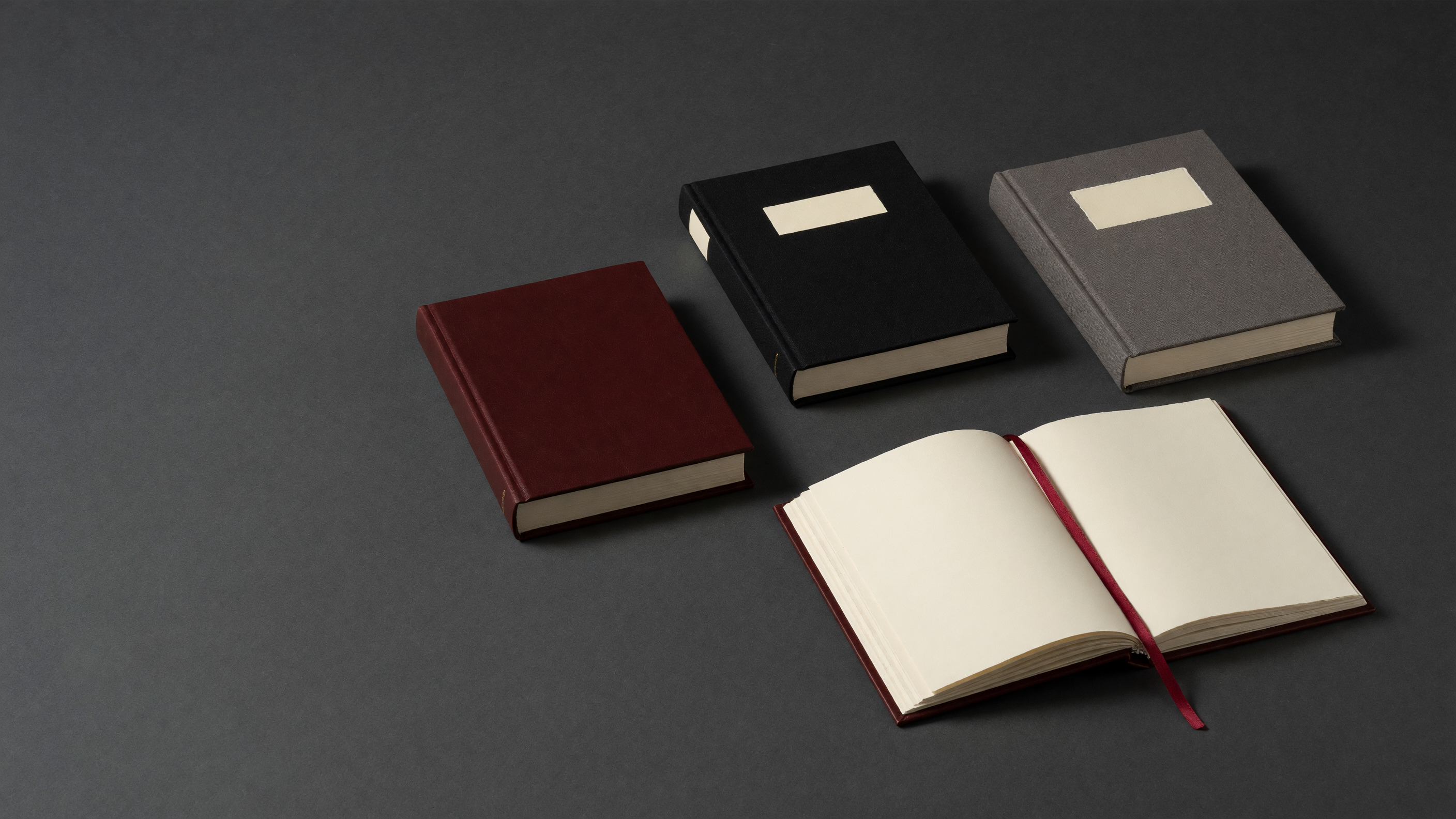 Three bespoke hardbound books and one open book arranged on charcoal paper.